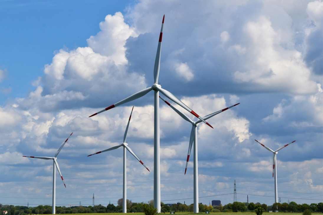 Windparkanlage mit fünf Windkraftanlagen vor bewölktem Himmel