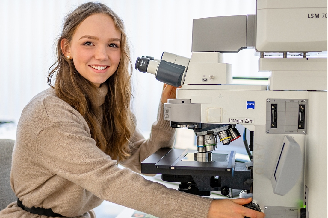 Eine junge Frau arbeitet mit Freude an einem Mikroskop im Labor.
