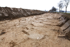 Foto: Bereits nach dem ersten Abzug mit der Baggerschaufel erkennt man im anstehenden Boden deutlich unterschiedliche Befunde, die  wahrscheinlich als vorgeschichtliche Siedlungsspuren gedeutet werden können. Eine präzisere Ansprache wird nach der Ausgrabung möglich sein.