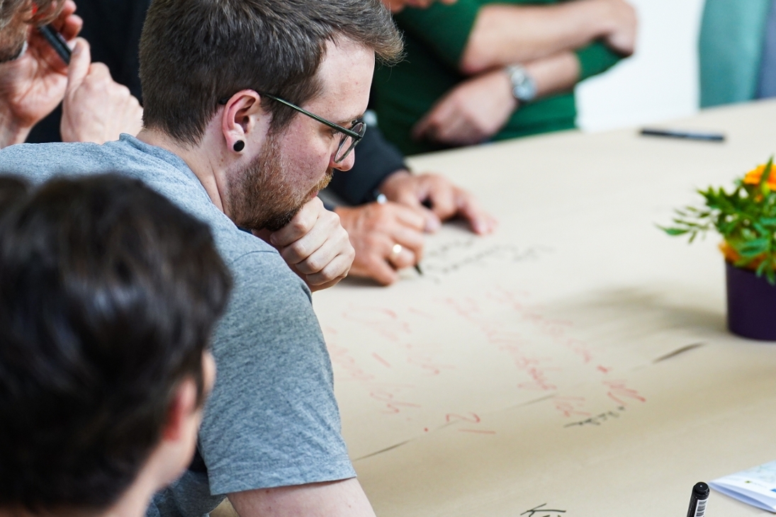 Teilnehmer eines Workshops notieren ihre Ideen und Gedanken auf ein großes Pergament auf einem der Diskussionstische.