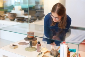 Foto: Kuratorin Linda Seifert betrachtet eine Vitrine mit Arbeitsmaterialien der Restaurierung wie Gipskleber und Pinsel.