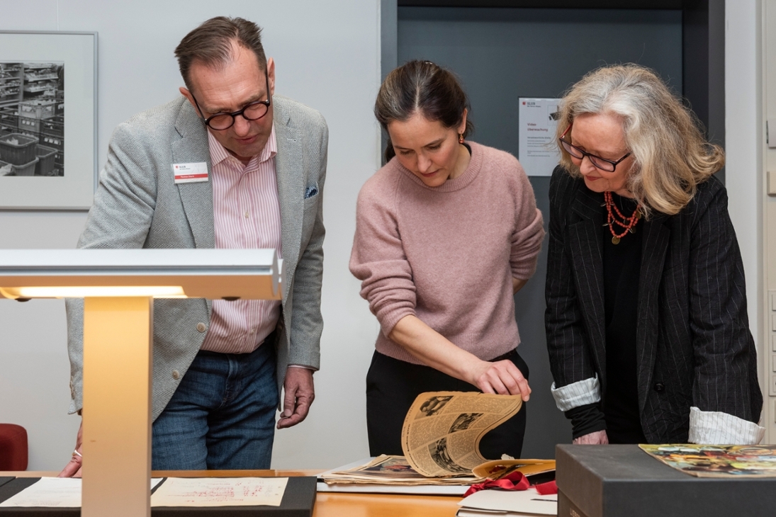 Thomas Stern (l., SLUB, Deutsches Archiv der Kulinarik) schaut mit Lilly Böhm und Maraike Wittbrodt (Mitte und rechts, Enkelin und Tochter von Ursula Winnington) auf ausgewählte Sammlungsstücke aus deren Nachlass.